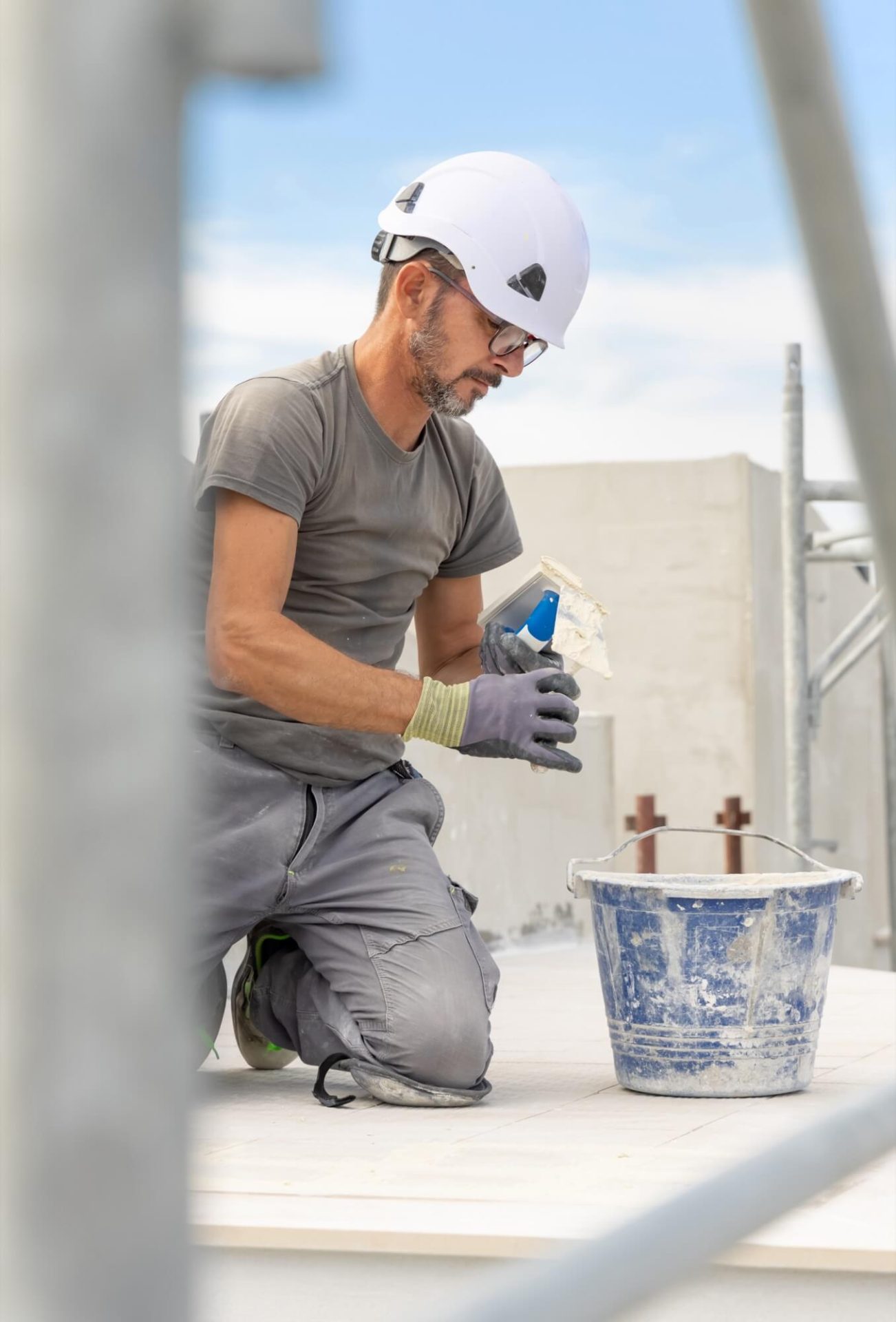 Knästående på marken, arbetar en hantverkare med fasadrenovering, klädd i skyddshjälm och handskar, med murbruk och verktyg nära till hands